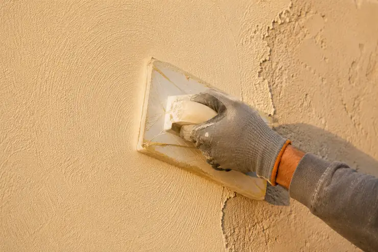 Artisan façadier appliquant un enduit taloché à la taloche, geste circulaire dans la matière fraîche