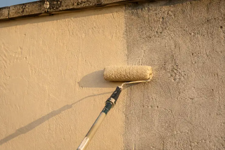 Application de peinture de façade au rouleau : contraste entre le mur repeint et le support ancien